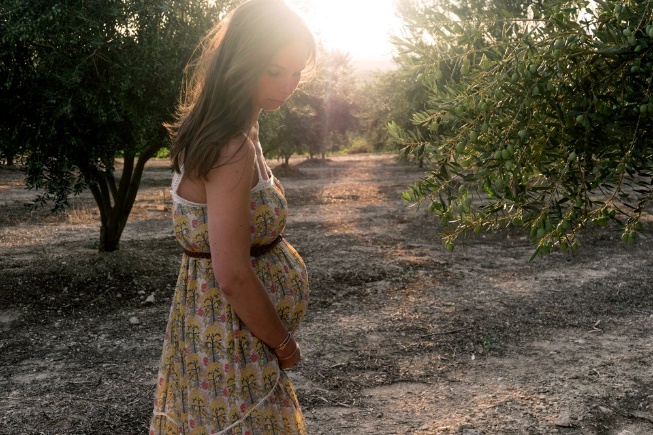 pregnant woman wearing beige and red floral sleeveless dress standing near plant