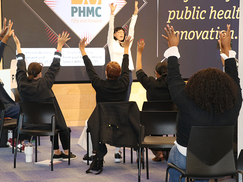 Audience members raise hands while a presenter stands on stage at the 2025 Mental Health Youth Summit