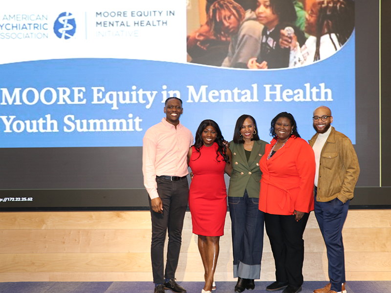 Five speakers pose on stage at the Moore Equity in Mental Health Youth Summit in front of a presentation screen