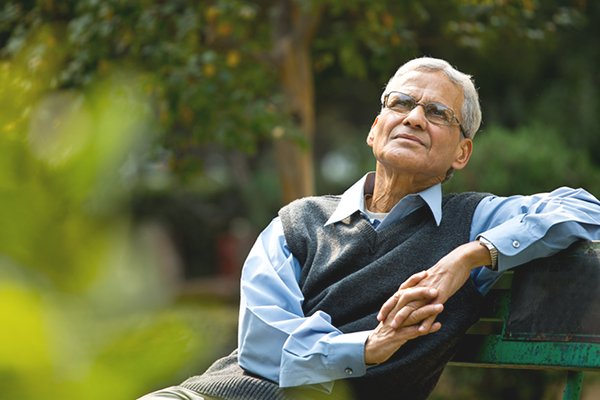 An older gentleman reclining on a park bench staring pensively into the sky.