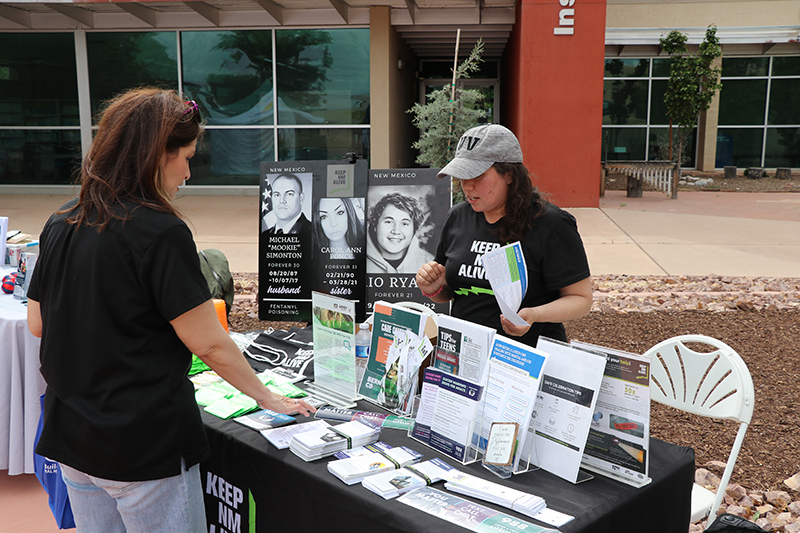Community member speaks with a health fair exhibitor at a resource table with brochures and information