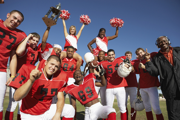 Football players, cheerleaders, and coach celebrating with trophy