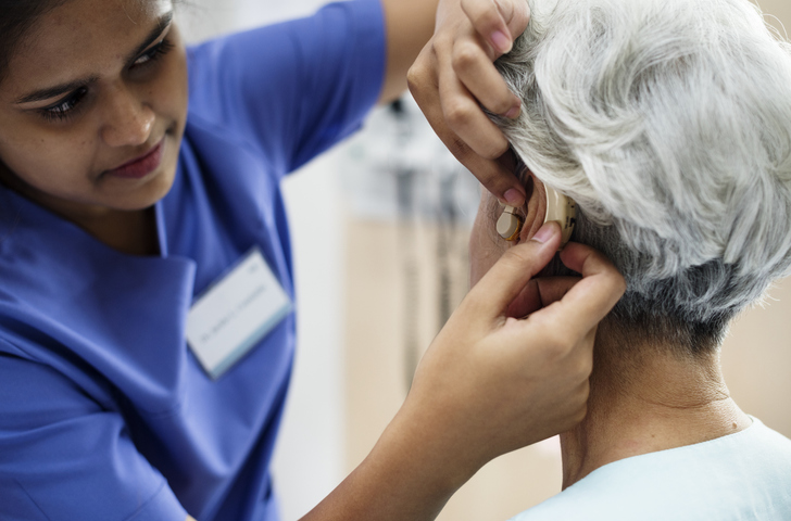 Nurse fitting a hearing aid on an elderly woman